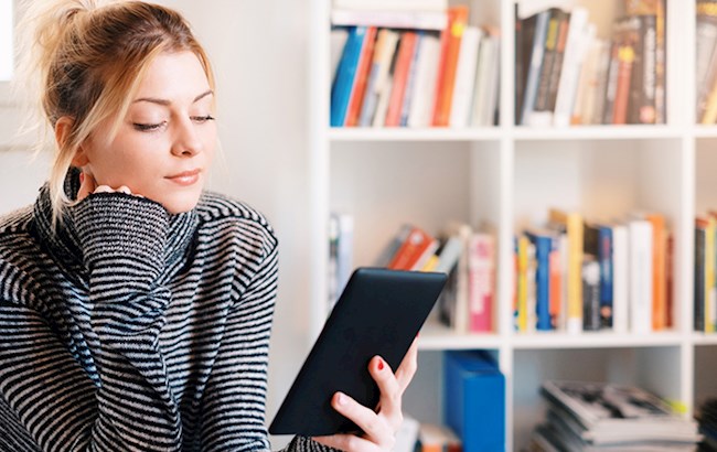 Woman reading eReader with bookcase behind her