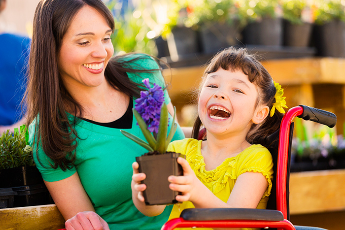 Happy child in a wheelchair holding a potted plant with her mother