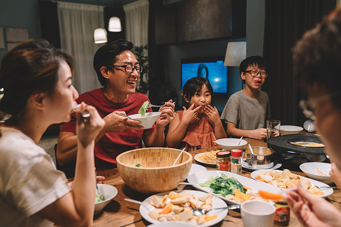 Family smiling sitting around dinner table eating food