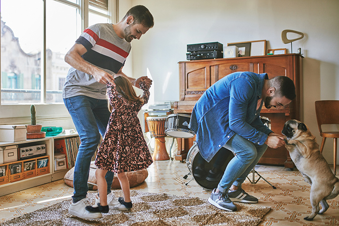 Parents dancing in living room with young girl and dog