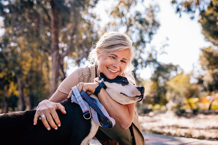 Older woman smiling outside embracing dog