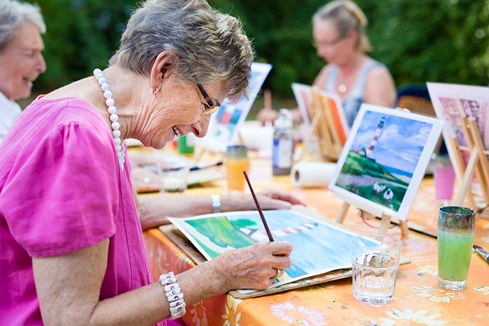 Three senior women outside at table painting lighthouses