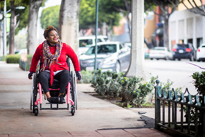 Woman smiling in wheelchair outside on city sidewalk