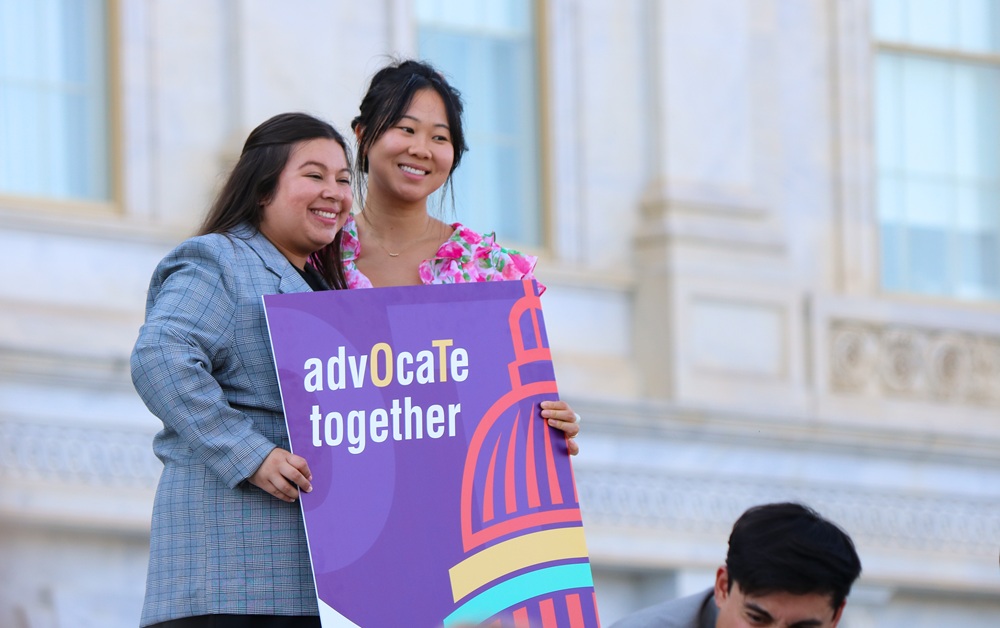 Two smiling women pose with sign on Capitol steps that reads Advocate Together
