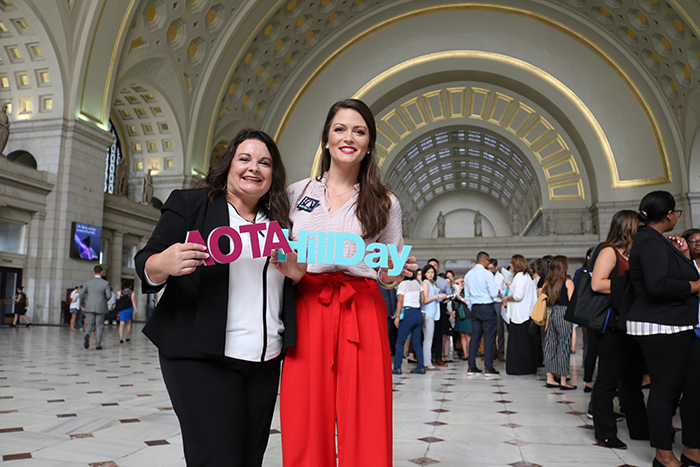 Two smiling women holding AOTA Hill Day signs inside building