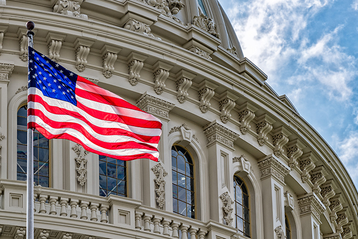 Close up shot of American flag waving on pole with US Capitol rotunda in the background