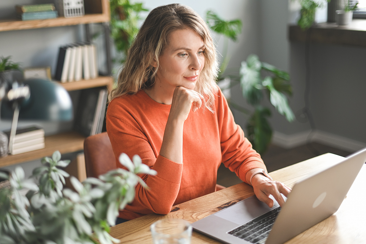 Woman using a laptop at a desk with her hand under her chin in thought