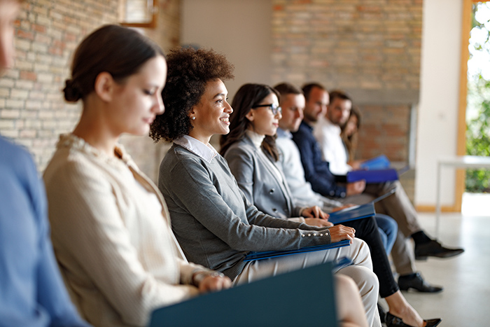 Professional men and women sitting along wall in chairs waiting for job interview