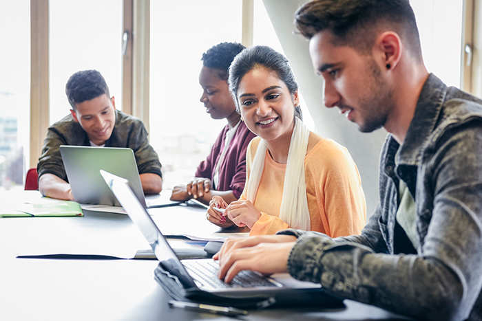 Two men and two women working at table together with laptops