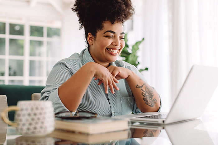 Happy woman looking at laptop screen with book on table 