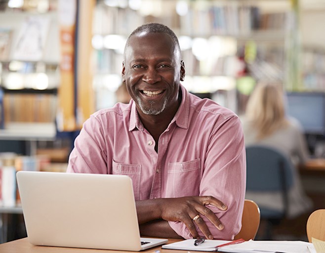 Smiling older man with open laptop looking at camera inside library