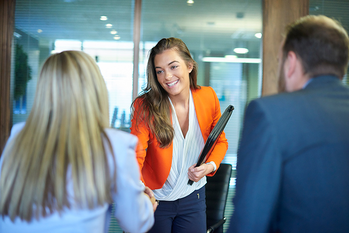 Smiling woman holding portfolio shaking hand with another woman and man at job interview