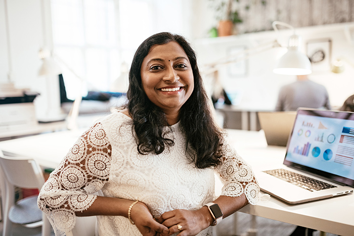 Woman smiling looking at camera with open laptop on table in background