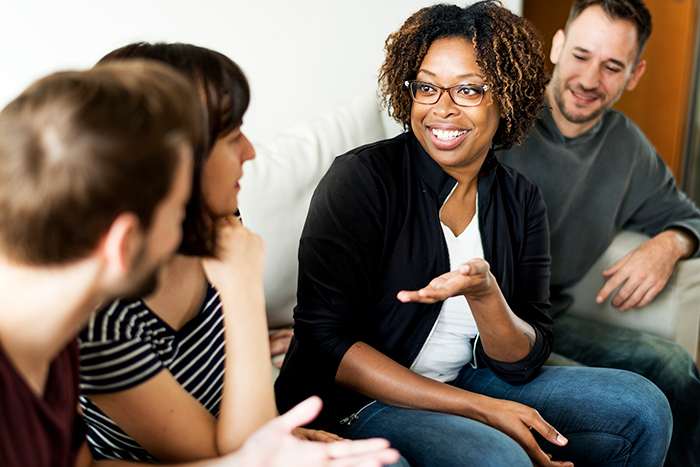 Two woman and two men sitting on couch talking with focus on smiling woman