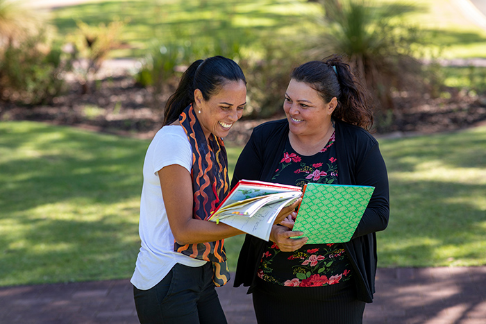 Two smiling woman talking outside looking at notebooks