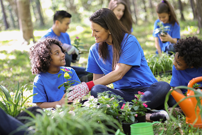 Woman planting flowers with two kids outside with others gardening in the background
