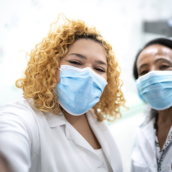 Two healthcare workers wearing face masks taking selfie and giving thumbs up