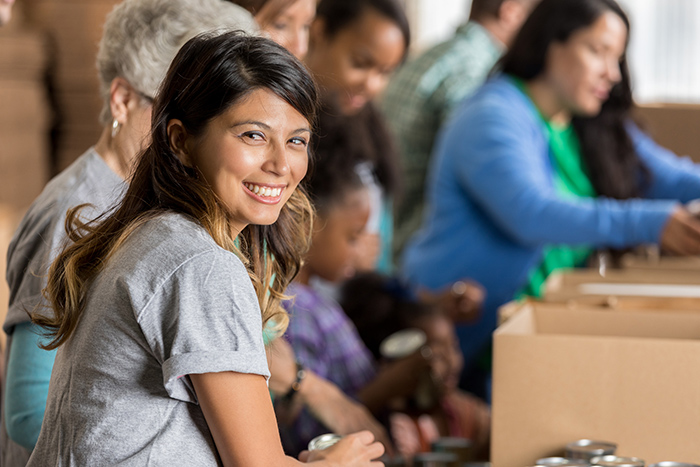 Woman smiling filling boxes with canned goods alongside other people in the background