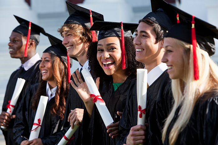 Diverse group of happy friends in graduation attire holding diplomas