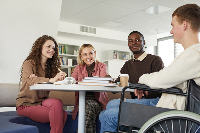 College friends studying around table with male in wheelchair in the foreground