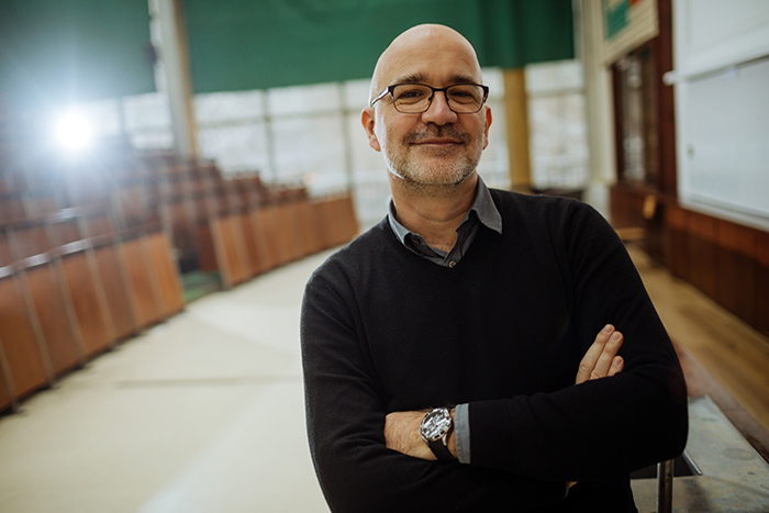 Smiling male college professor with arms crossed inside an empty lecture hall