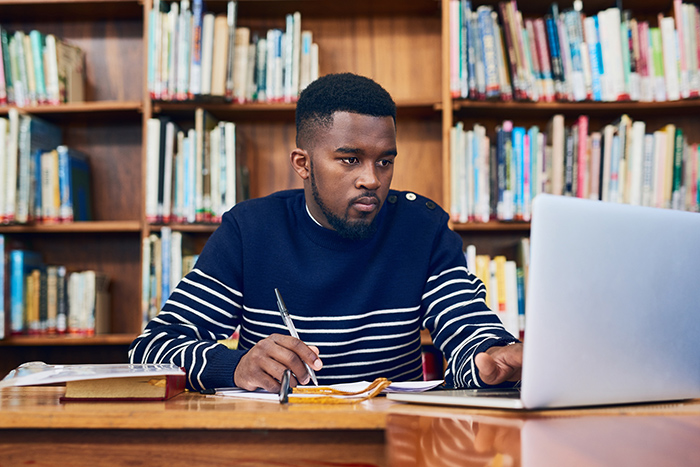 Male college student studying on laptop in library