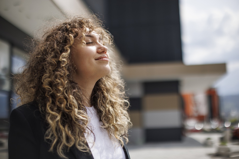 woman closing her eyes and looking up at the sky while standing outside
