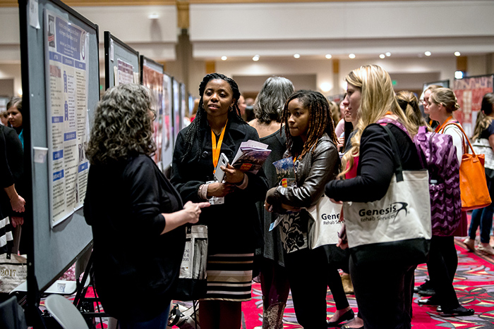 Woman speaking to female AOTA Annual Conference and Expo poster session attendees