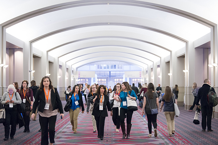 People walking down hallway at AOTA Annual Conference and Expo with tote bags