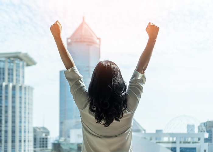Back of a woman with arms up in the air celebrating success with city in background