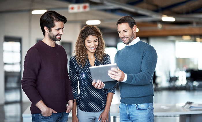 Two men and a female in office looking at tablet