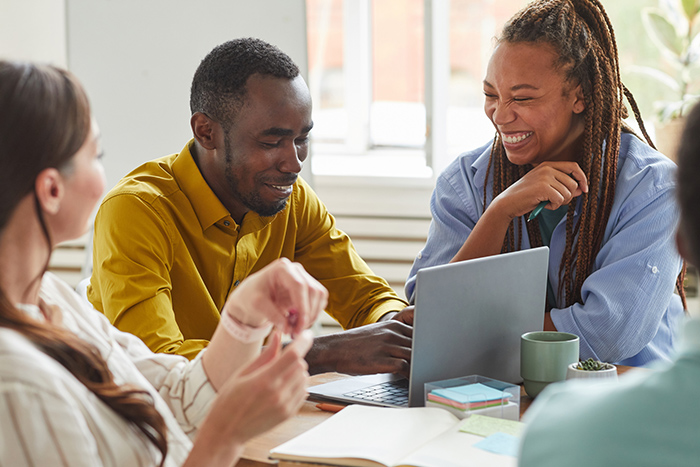 Man and woman working together at table with laptop and other people
