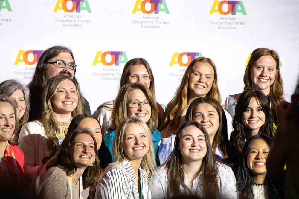 Smiling group gathers for photo against AOTA logo backdrop