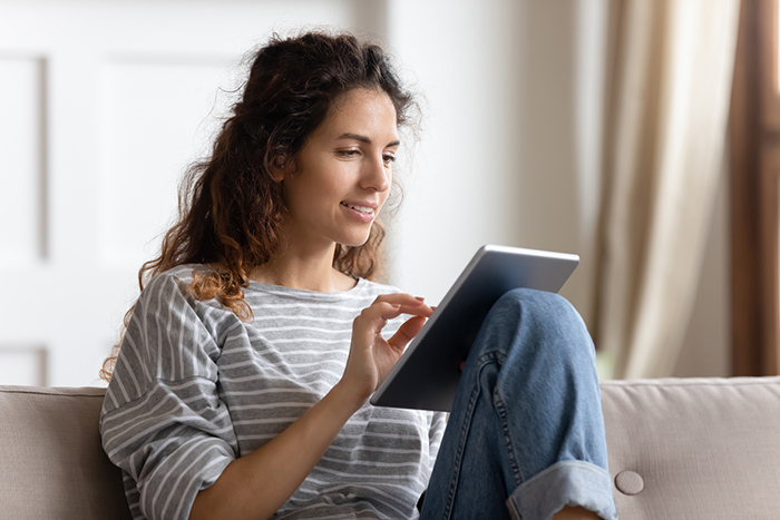 Woman sitting on couch inside reading tablet