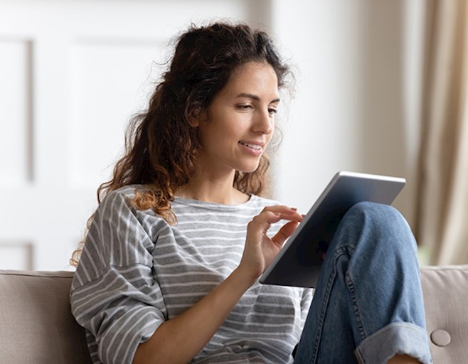 Woman sitting on couch inside reading tablet