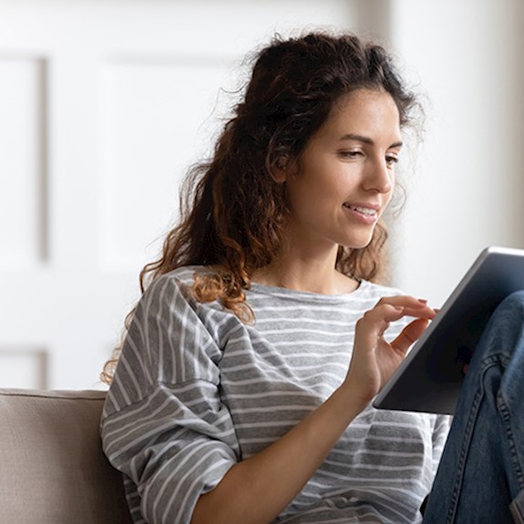 Woman sitting on couch inside reading tablet