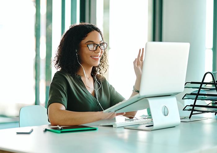 Smiling woman waving at computer during virtual meeting