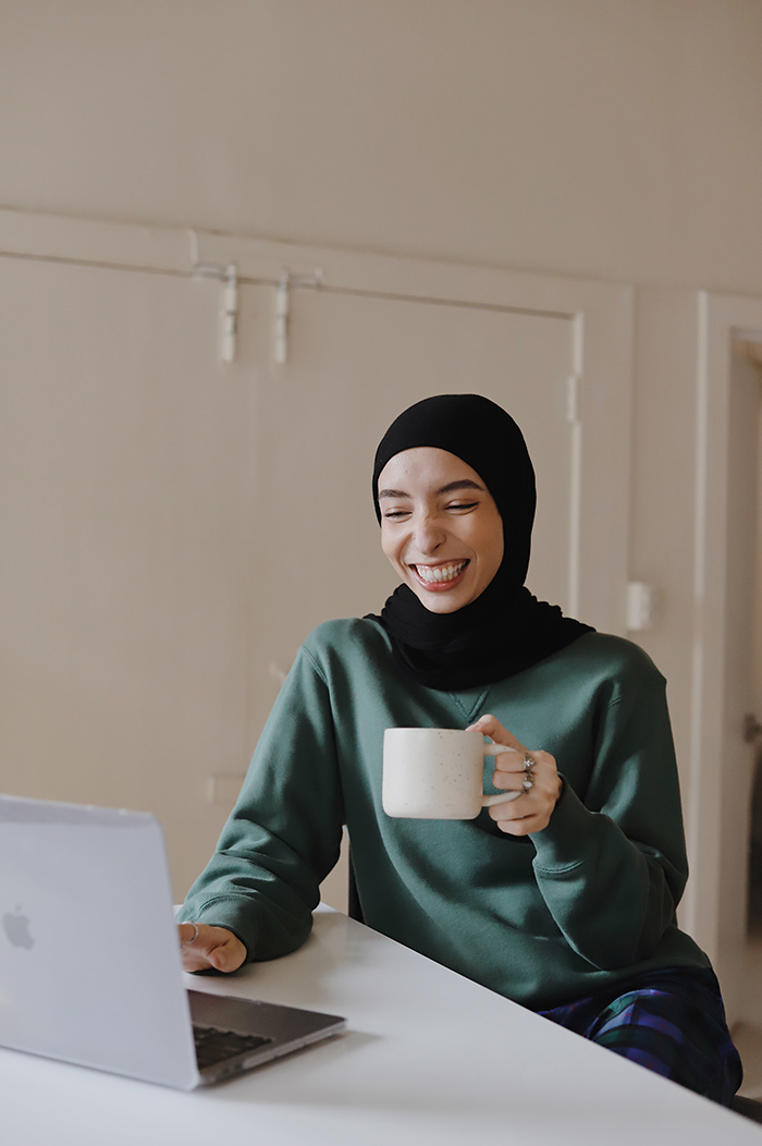 Smiling woman working on computer at table while drinking coffee
