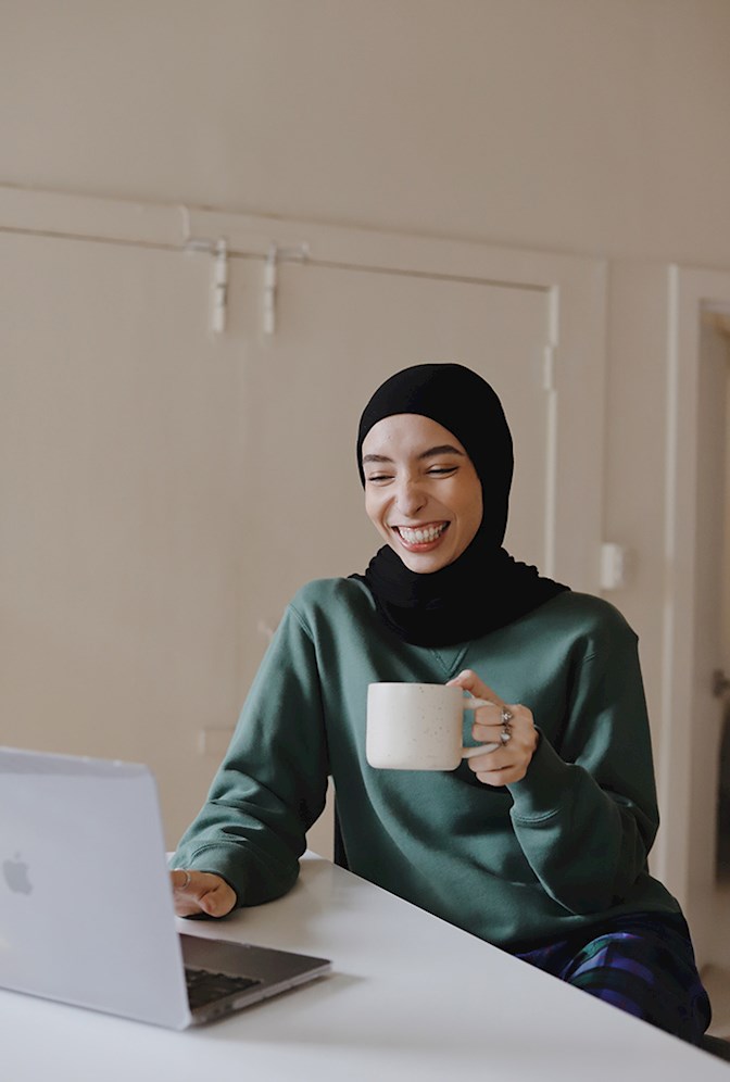 Smiling woman working on computer at table while drinking coffee