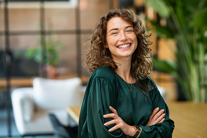 Smiling woman with arms crossed looking at camera inside office
