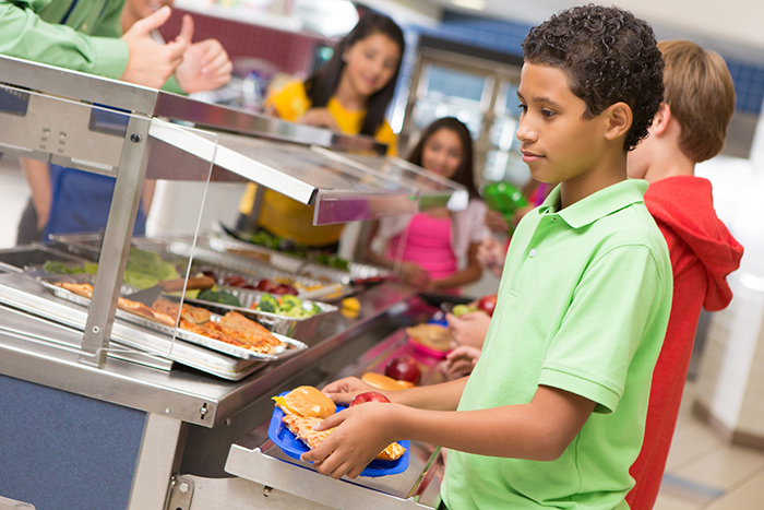Boy in cafeteria line at school with classmates and a tray of food
