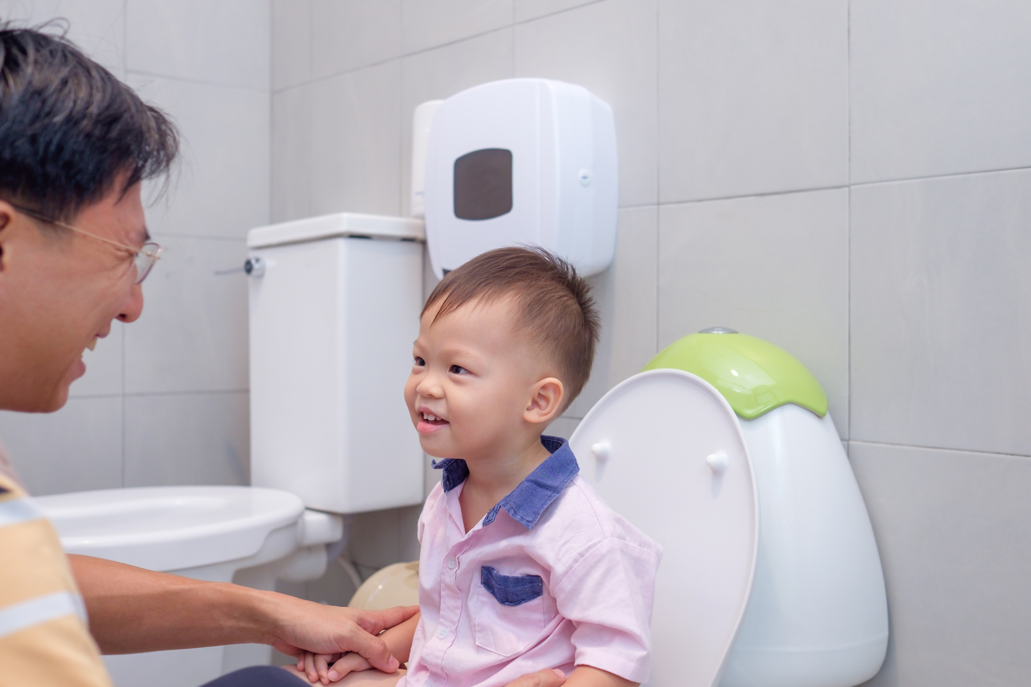 Toddler and adult in bathroom. Child sits on potty training seat.