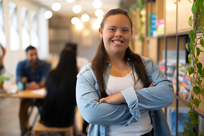 Woman smiling at camera with arms crossed and coworkers in background