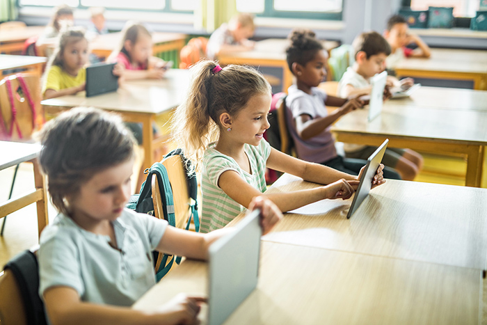 Children in classroom sitting at desks using tablets