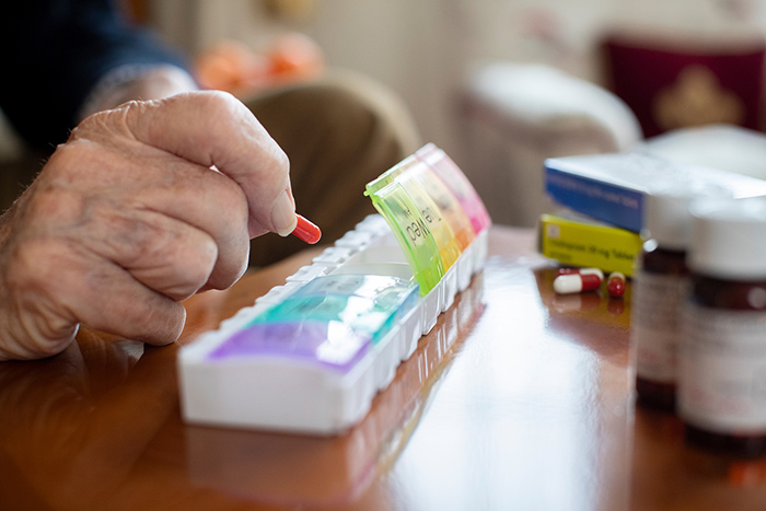 Close up of an elderly mans hands putting pills into pill case with other medication on table