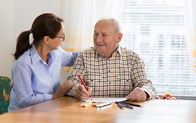 Senior man holding red pencil with female occupational therapist working on handwriting