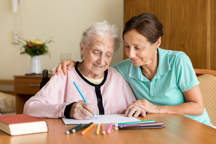 Female occupational therapist alongside senior woman holding a pencil working on handwriting skills