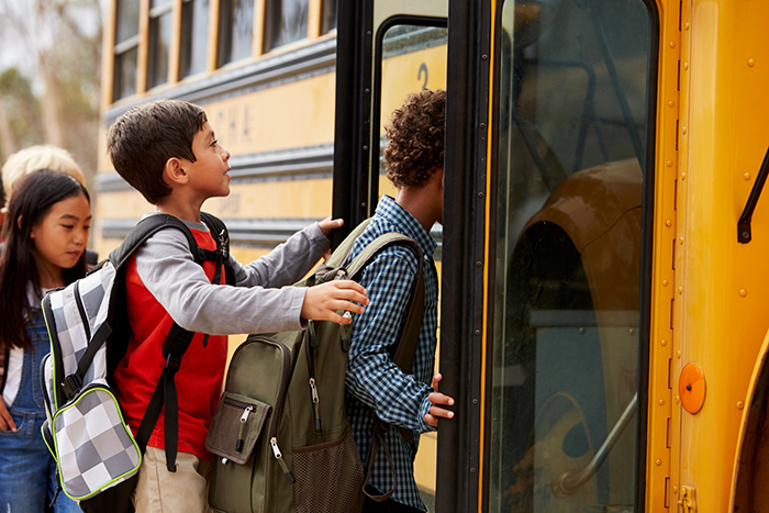 Three school aged kids wearing backpacks and entering school bus