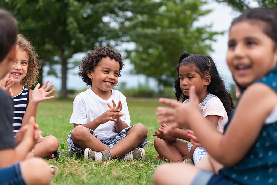 Diverse group of preschool kids sitting in circle outside laughing