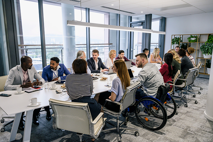 Large conference table full of professional people talking with one man sitting in a wheelchair